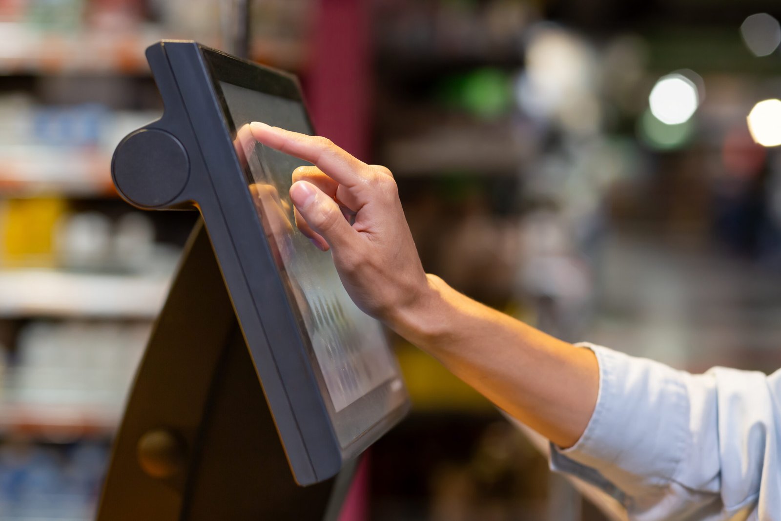 Close-up photo of a woman’s hand in a supermarket inside using a self-service scale weighing vegetables and fruit in the store